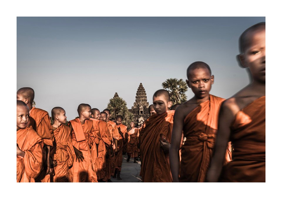A line of Buddhist monks in saffron robes exiting an ancient stone gateway on a private Angkor Wat photography workshop.