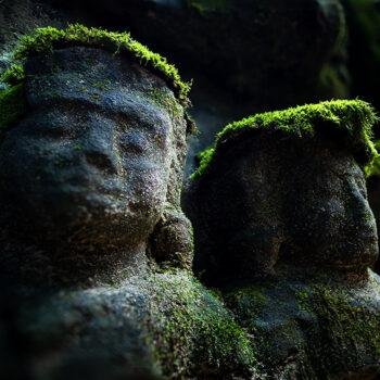Ancient stone heads of bridge statues covered in vibrant green monsoon moss with dramatic side lighting during a private Siem Reap photography workshop.